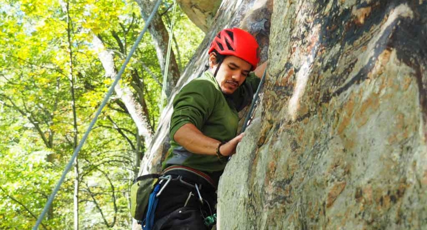 A person wearing safety gear is secured by ropes as they rock climb